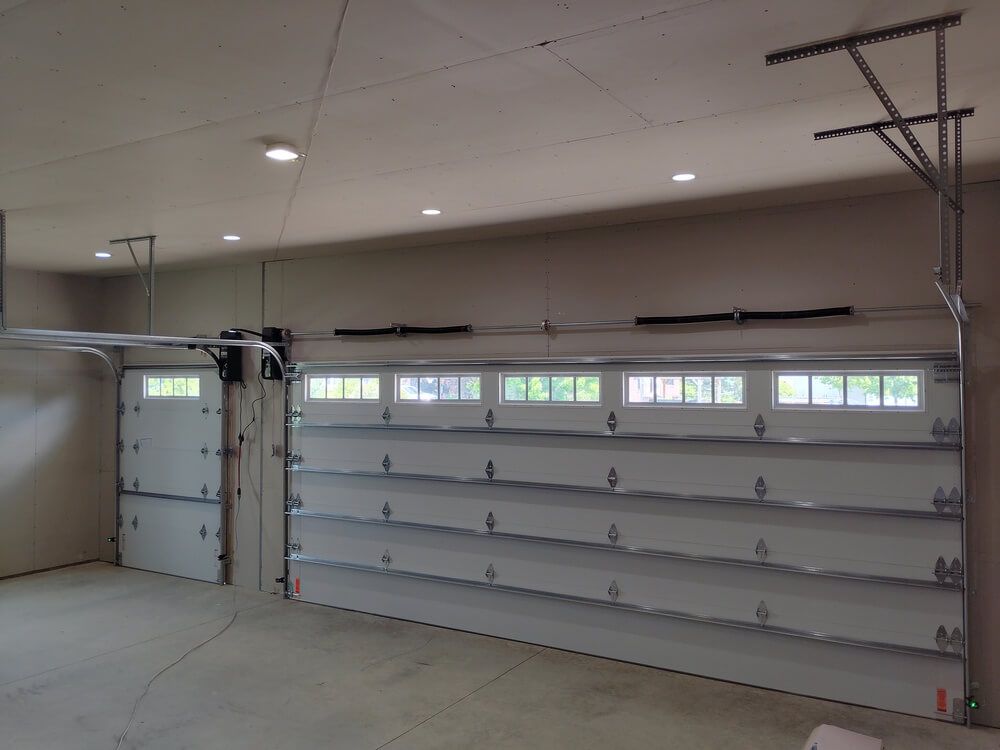 Empty garage with a closed door, wall-mounted shelves, and ceiling lights.