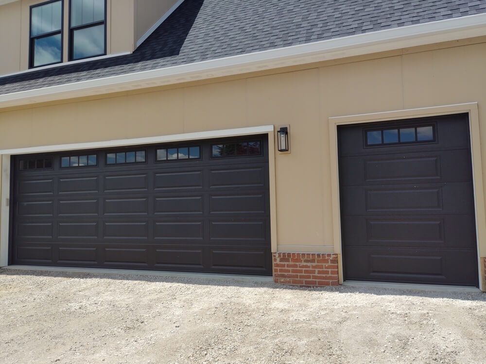 Two dark garage doors on a beige house exterior with brick accents and a shingled roof.