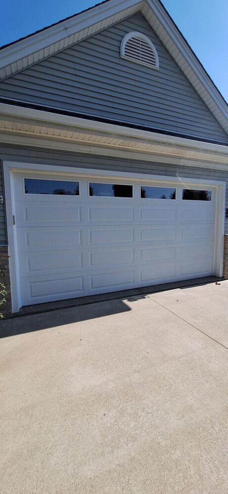 White garage door on a beige house with a small arched attic vent and concrete driveway.