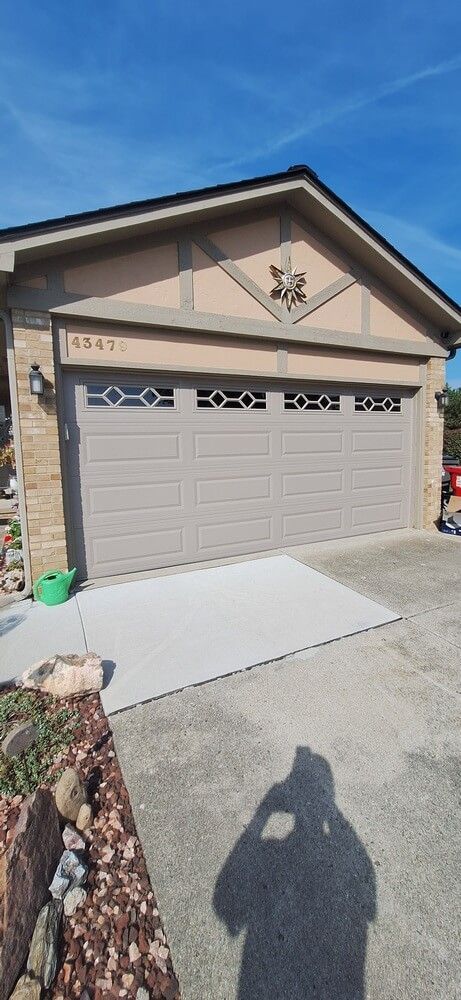 Single-car garage with tan siding, stone trim, and a concrete driveway under a blue sky