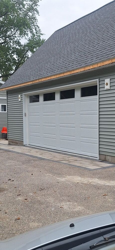 White garage door on a gray house with dark shingled roof and gravel driveway