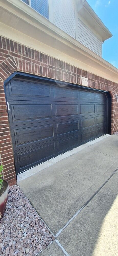 Black garage door on a brick house beside a concrete driveway
