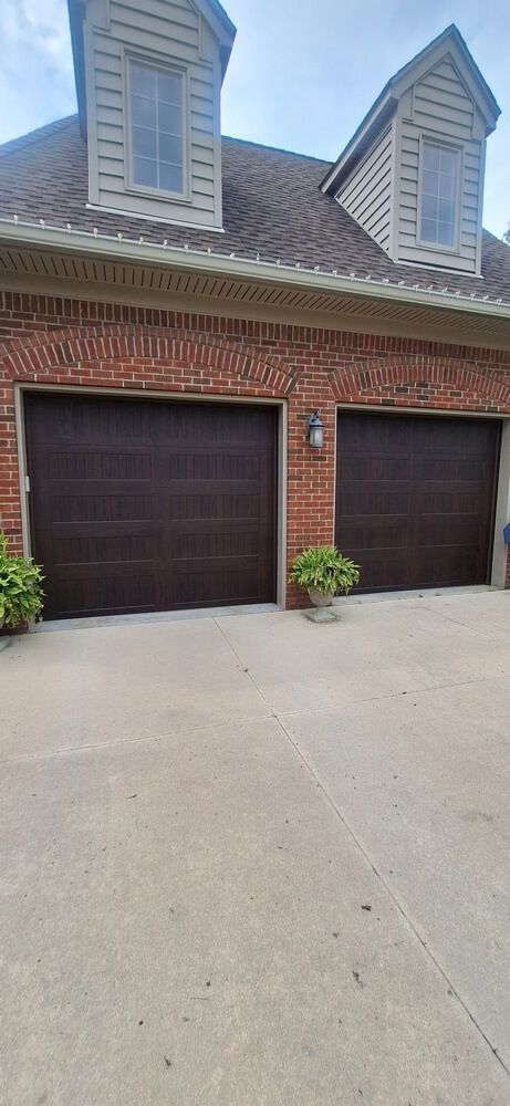 Brick house with two dark garage doors and dormer windows above a concrete driveway