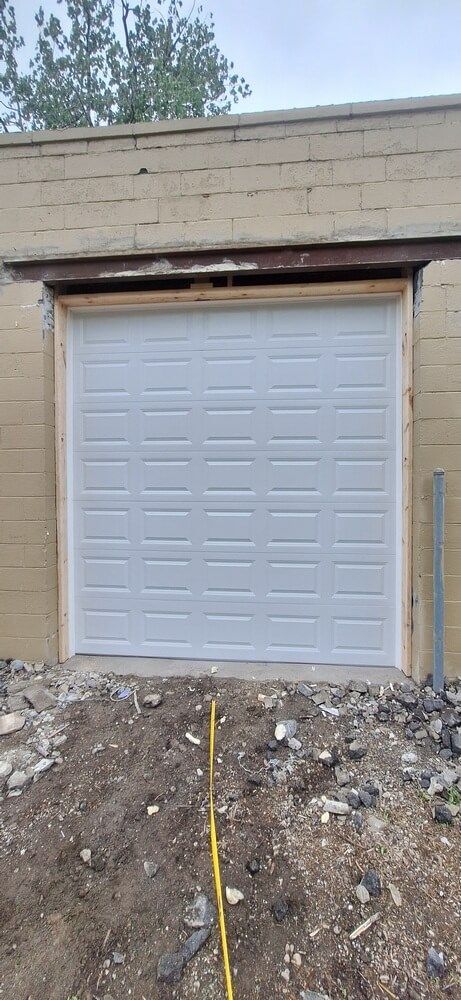 White garage door set in a tan building, with gravel and a yellow tape line in the foreground.