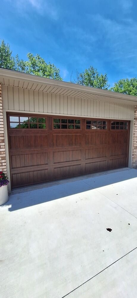 Brown garage door under a beige roof with blue sky and concrete driveway
