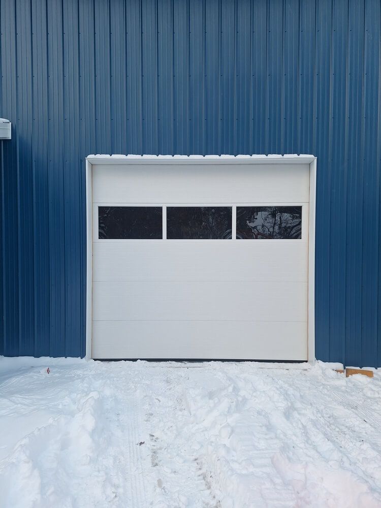 White garage door in a blue building with snow-covered ground in front.