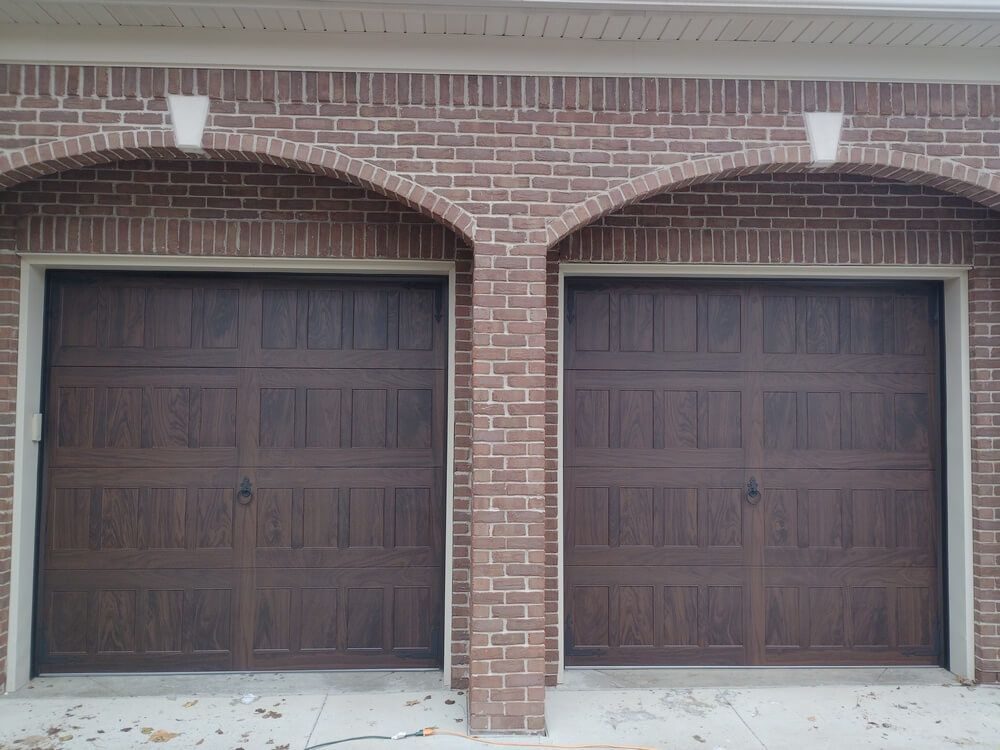 Two dark brown garage doors on a brick house exterior