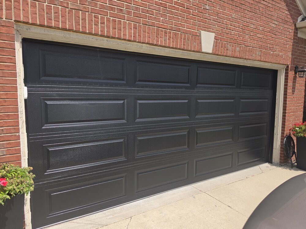Black double garage door on a brick house, viewed from a driveway.