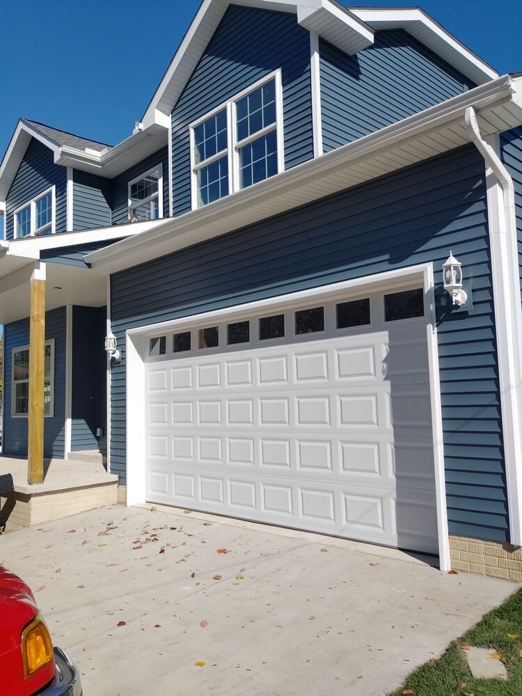 Blue house with white garage door and trim, front porch, and concrete driveway under a clear sky