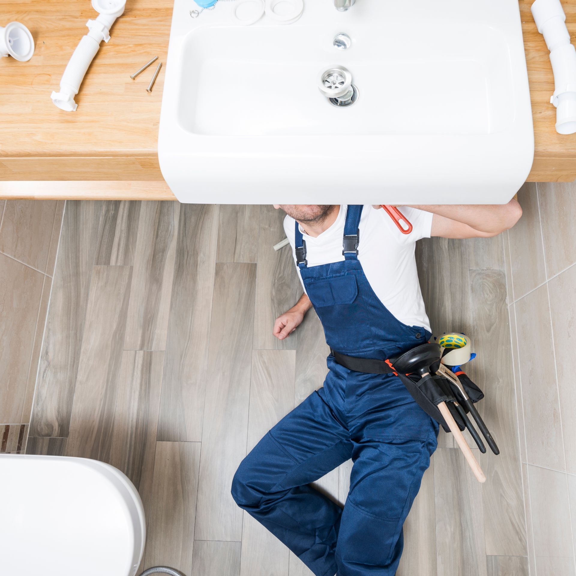 A plumber is laying on the floor under a sink in a bathroom.