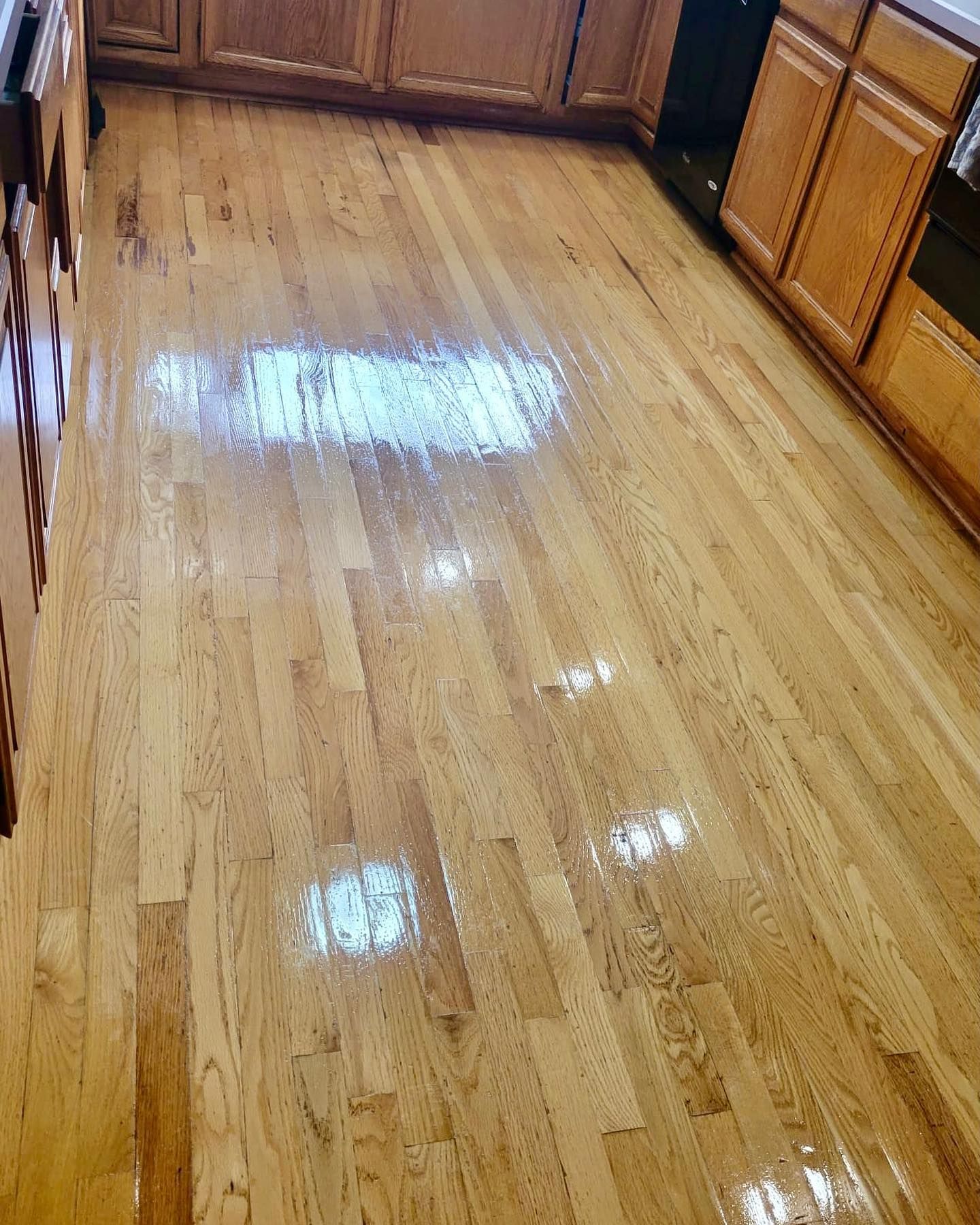 Polished hardwood kitchen floor with bright light reflections and wooden cabinets along the edges