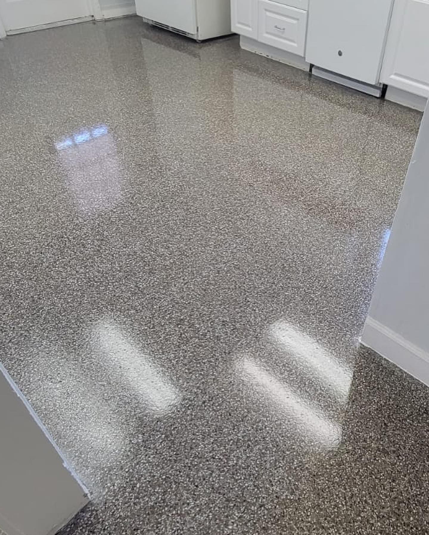 Shiny speckled epoxy floor in a bright kitchen with white cabinets and reflections of overhead lights