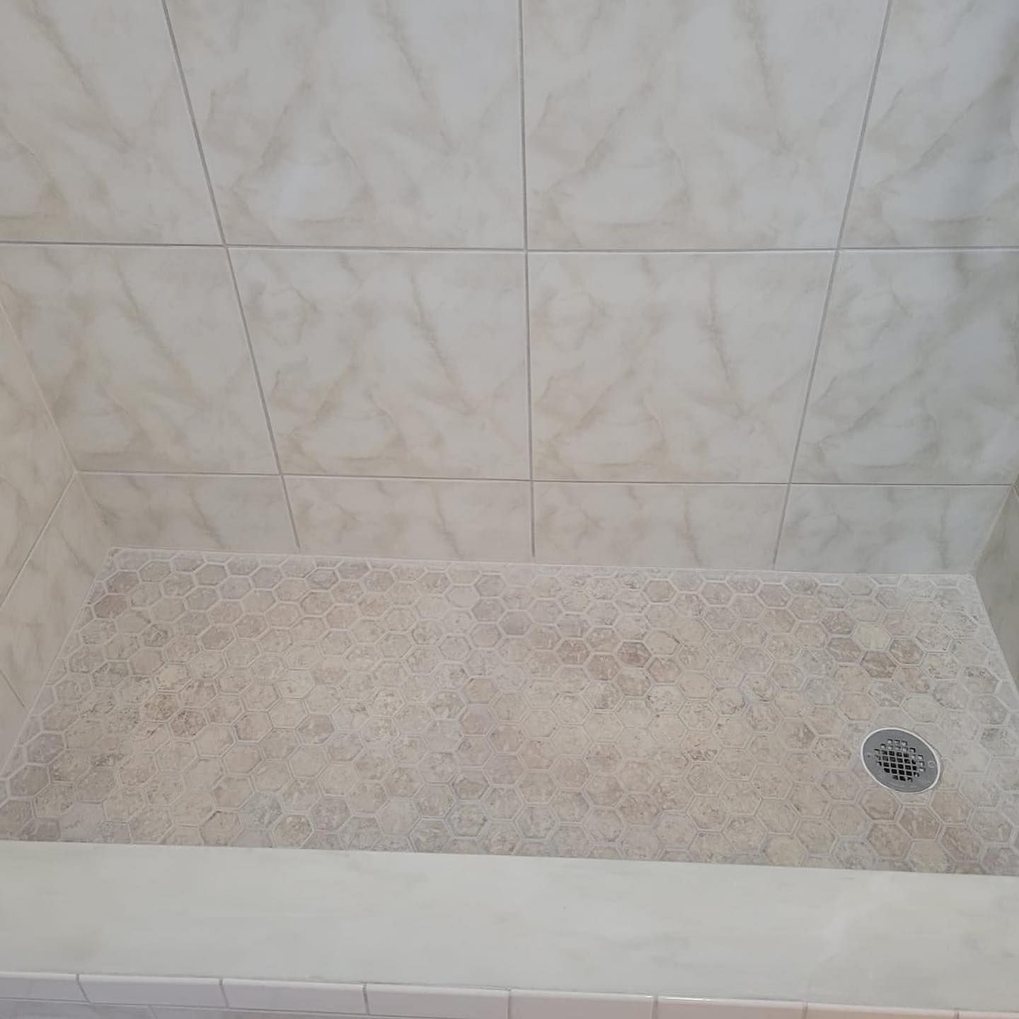 A shower stall with white tiles and a drain in a bathroom.