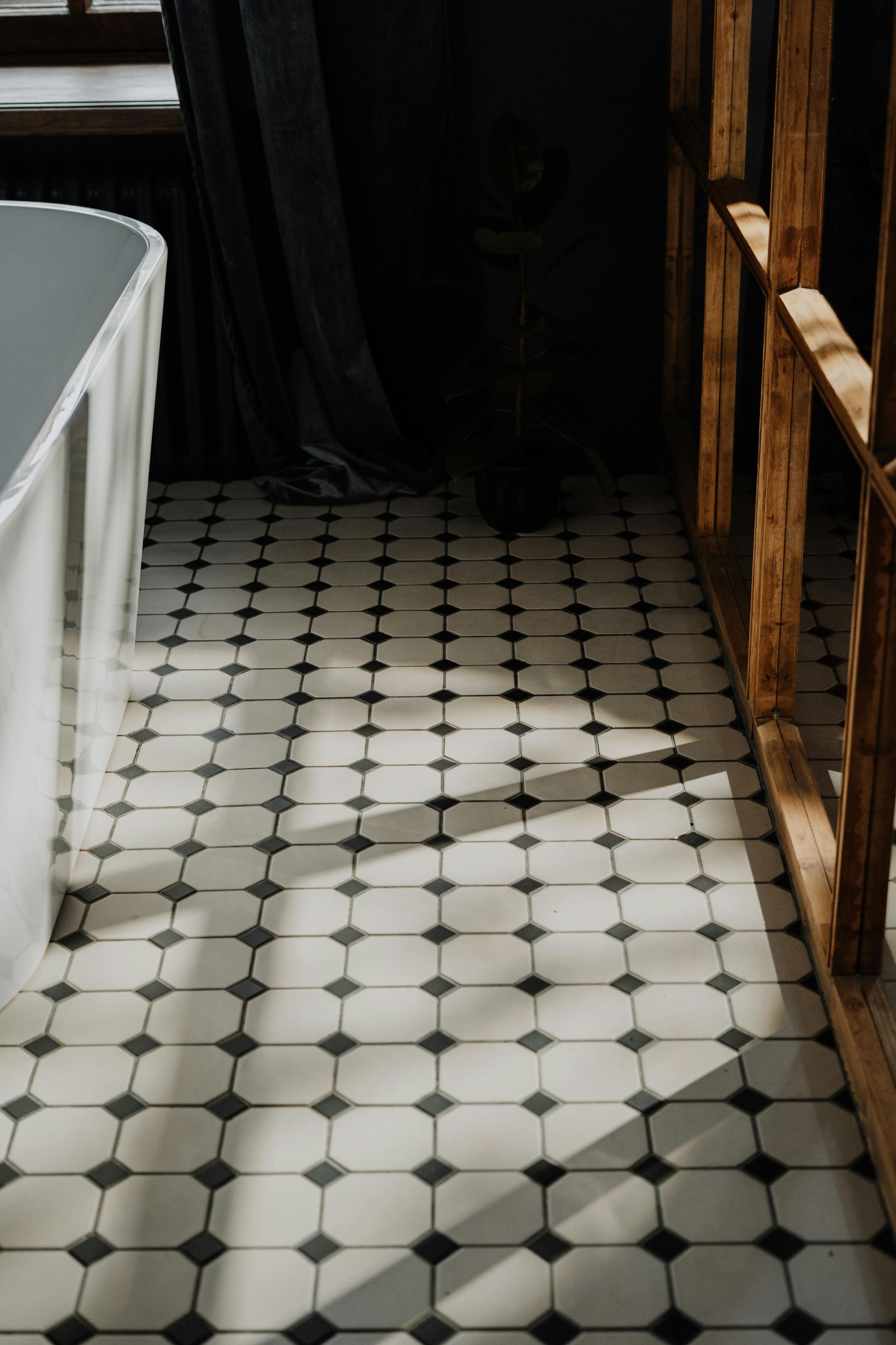 Black-and-white tiled floor in a sunlit hallway beside a tub and wooden wall.