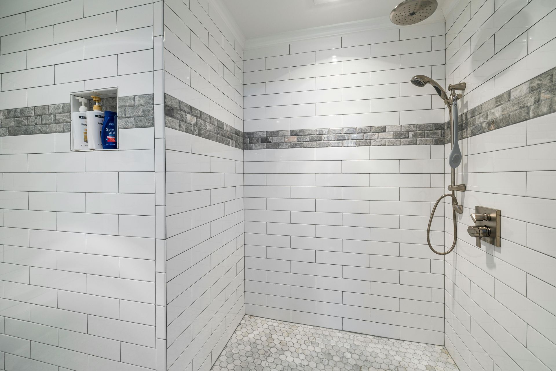 White tiled walk-in shower with handheld showerhead and built-in niche shelves