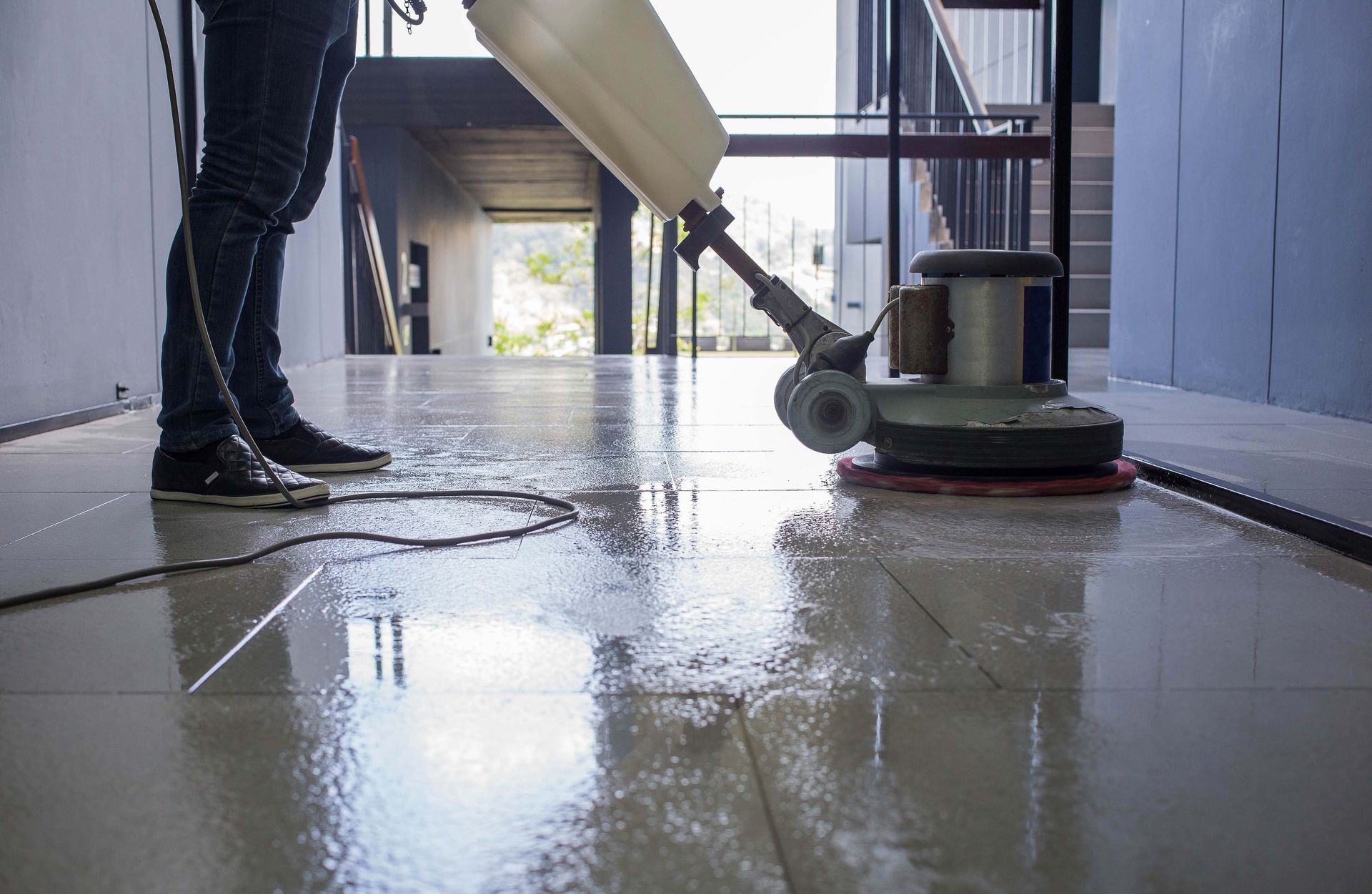 Person using a floor polisher on a wet indoor hallway floor