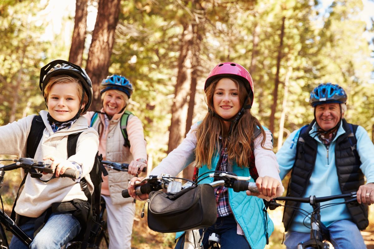 Family on bikes smiles in a forest setting, wearing helmets.
