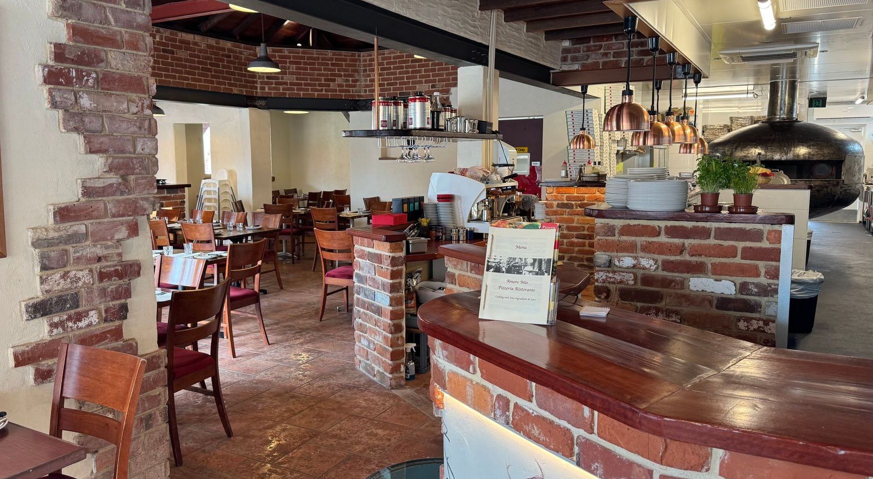Interior of a rustic restaurant with exposed brick walls, wooden tables, a pizza oven, and a bar.