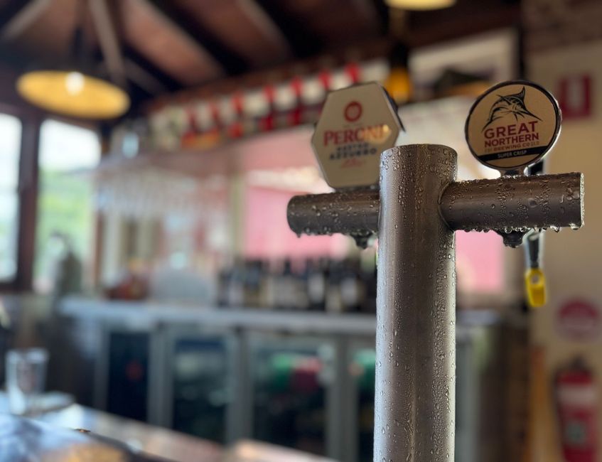 Close-up of a bar tap with condensation, in front of a blurry bar setting with beer taps and glasses.