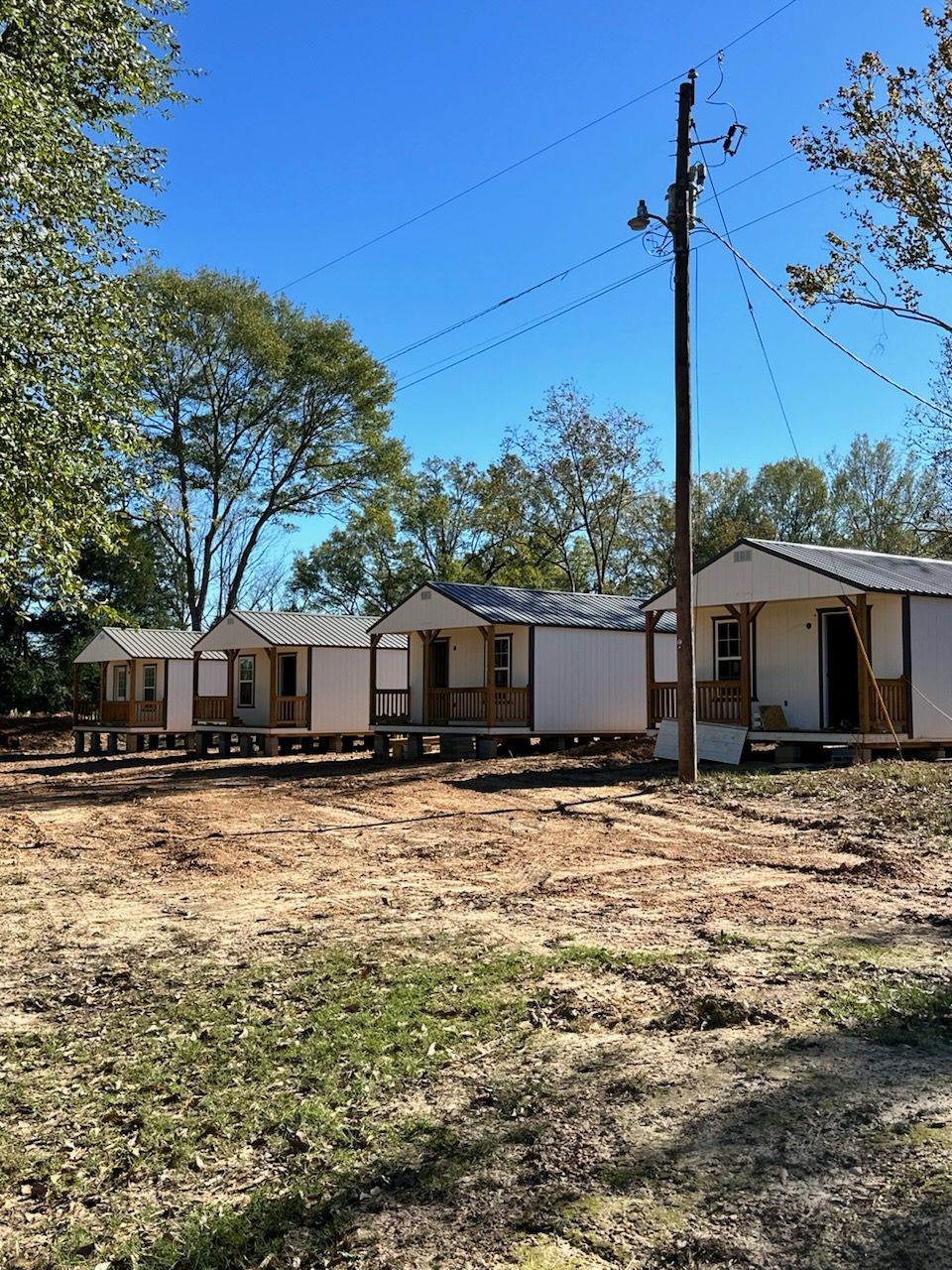 A row of small houses are sitting in a field next to a power pole.