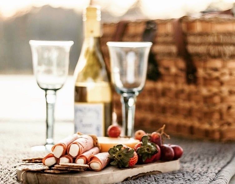 A wooden cutting board with a bottle of wine , glasses , crackers , strawberries and grapes on it.