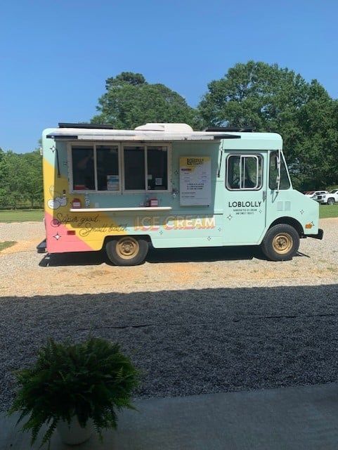 An ice cream truck is parked in a gravel lot.