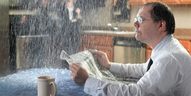 A man is sitting at a table reading a newspaper in the rain.