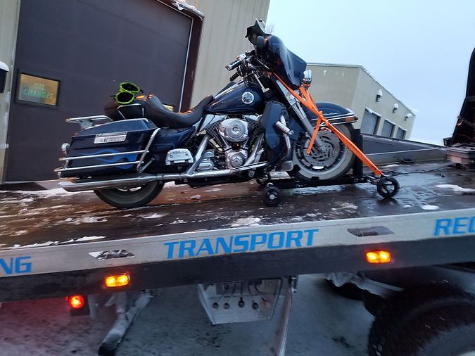 A motorcycle is sitting on top of a tow truck that says transport