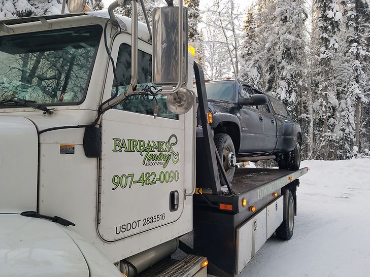 A tow truck with a car on the back is parked in the snow.