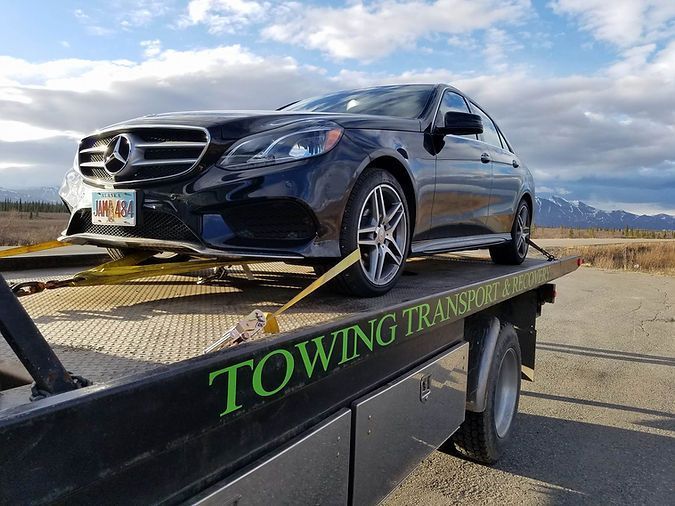 A black mercedes benz is sitting on top of a towing truck.
