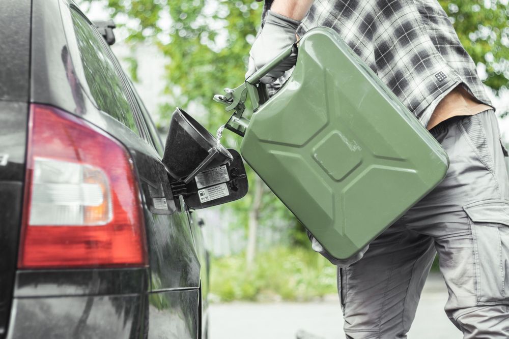 A man is loading gas into a car with a gas can.