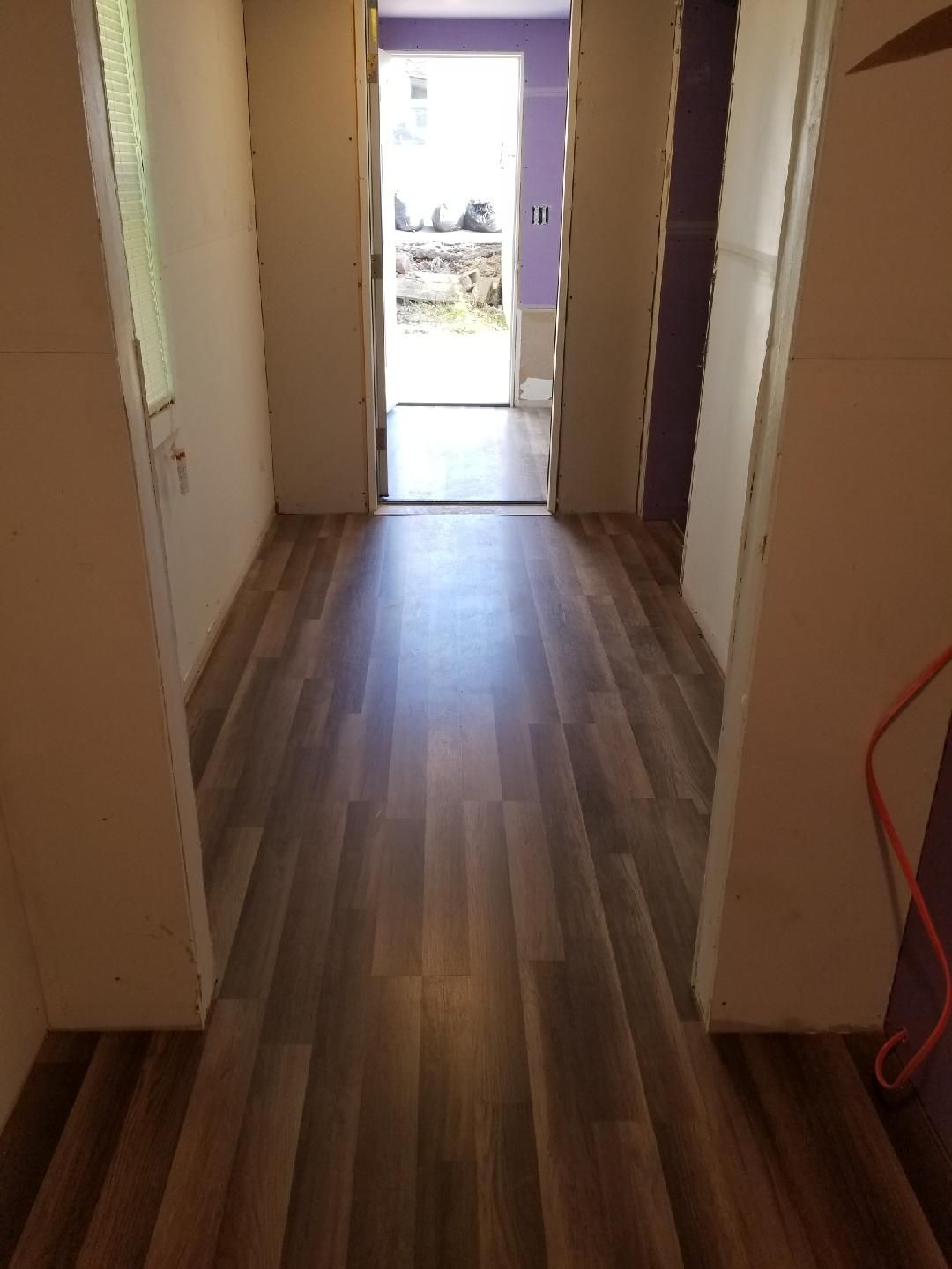 Narrow hallway with wood flooring leading to a bright open doorway.