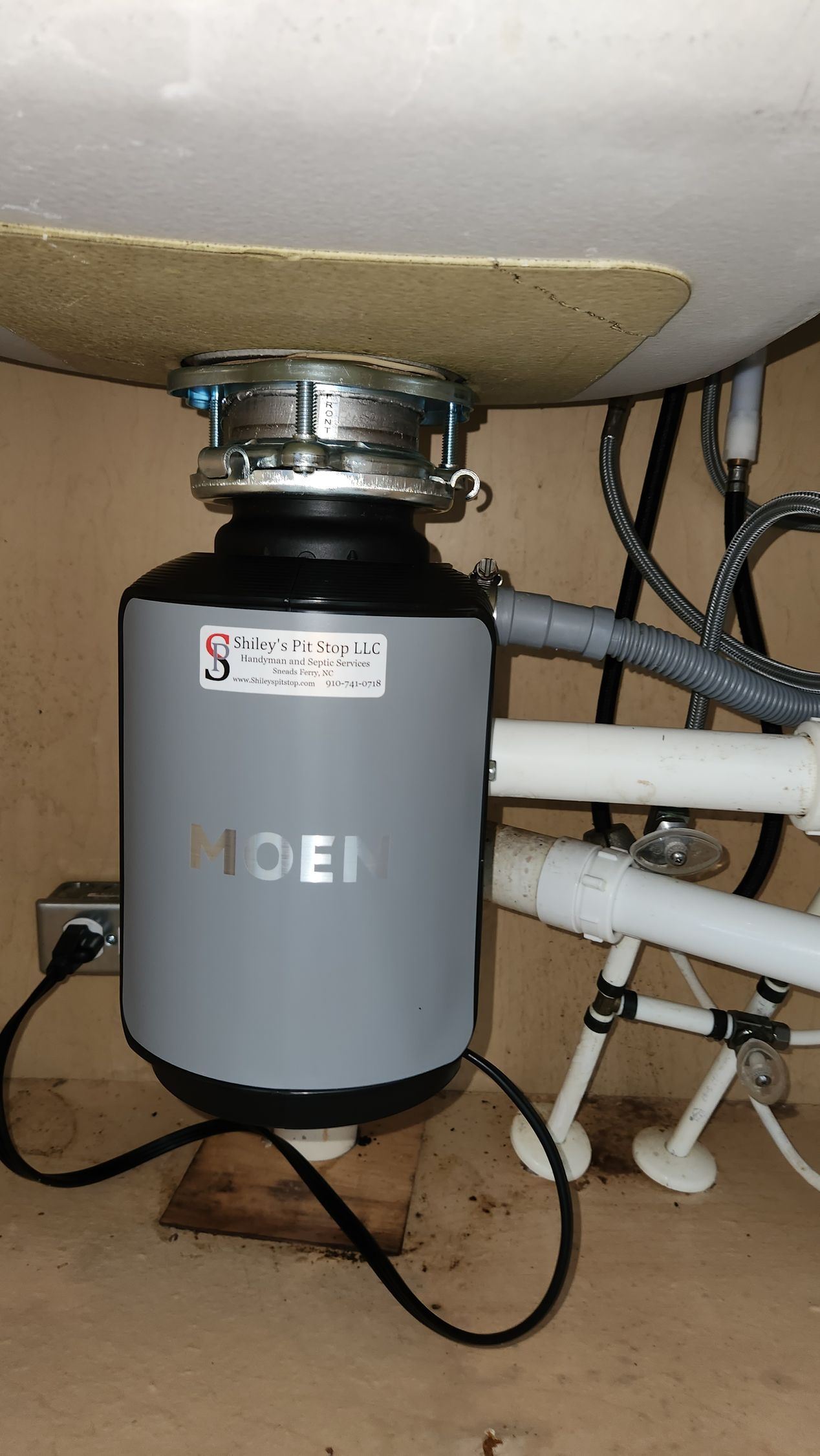 Under-sink garbage disposal with gray housing, pipes, and wiring in a cabinet