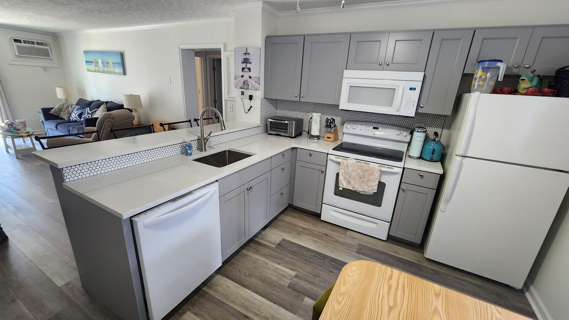 Bright kitchen with white appliances, gray cabinets, island sink, and wood-look flooring