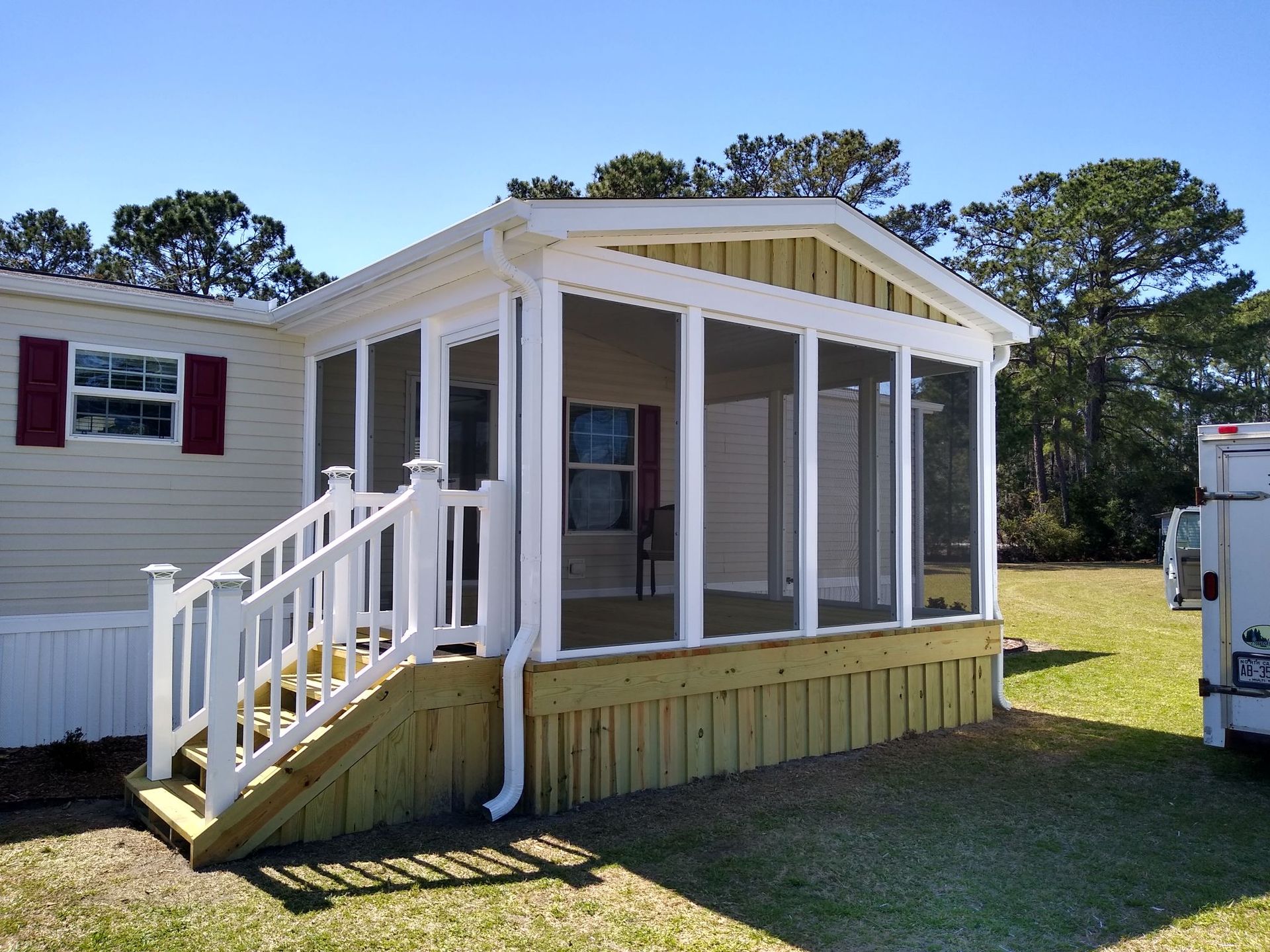 Small white porch with stairs on a mobile home in a grassy yard under a blue sky