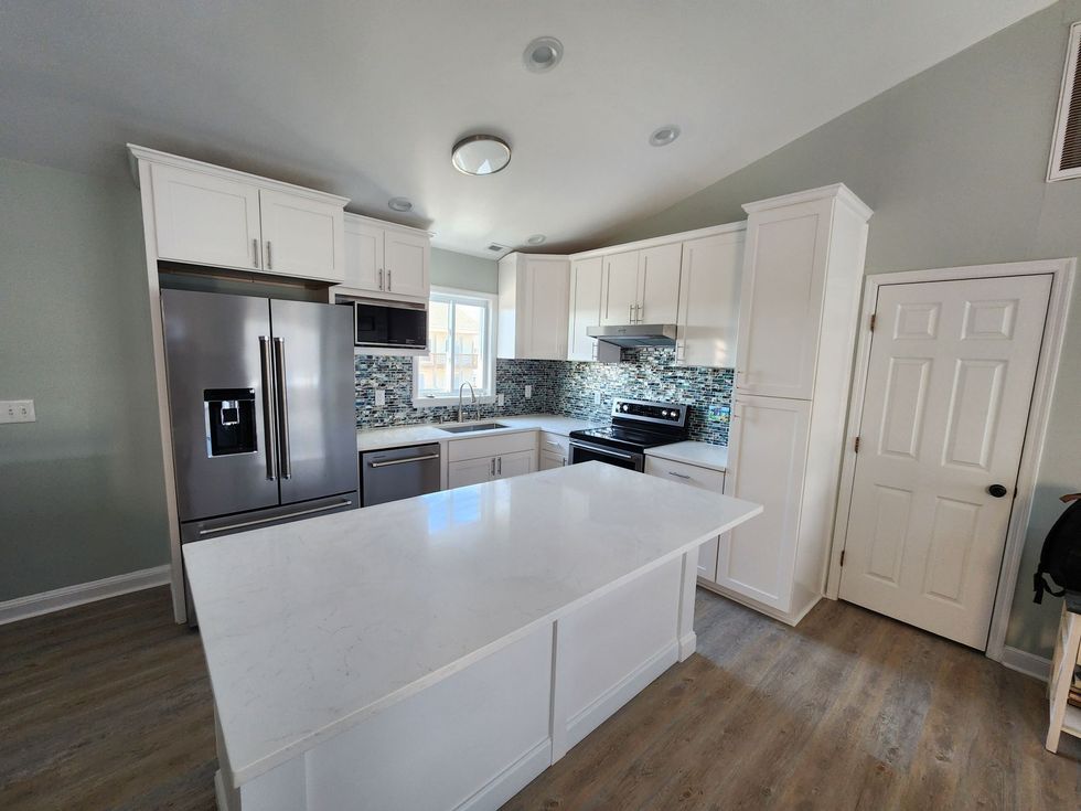 Bright white kitchen with island, stainless fridge, gray cabinets, and wood-look flooring.