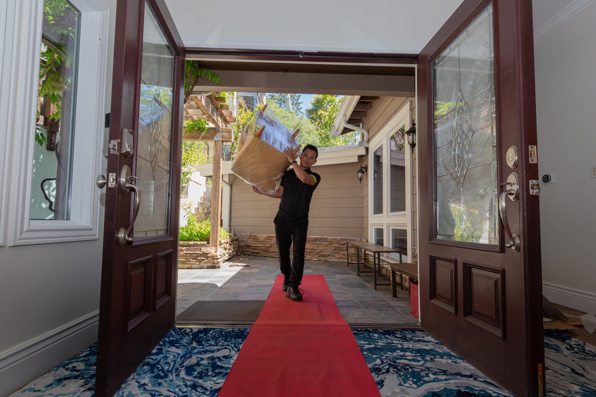 A man is carrying a box on a red carpet into a house.