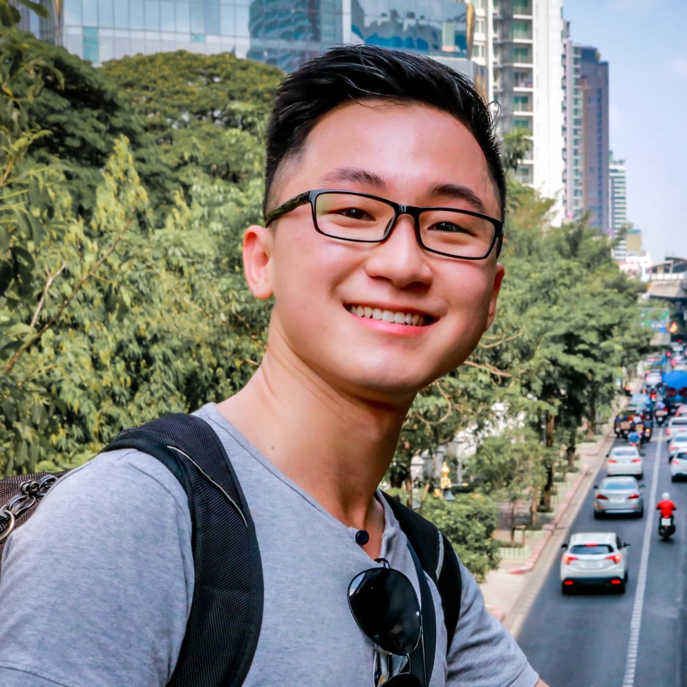 A young man wearing glasses and a backpack is smiling for the camera.