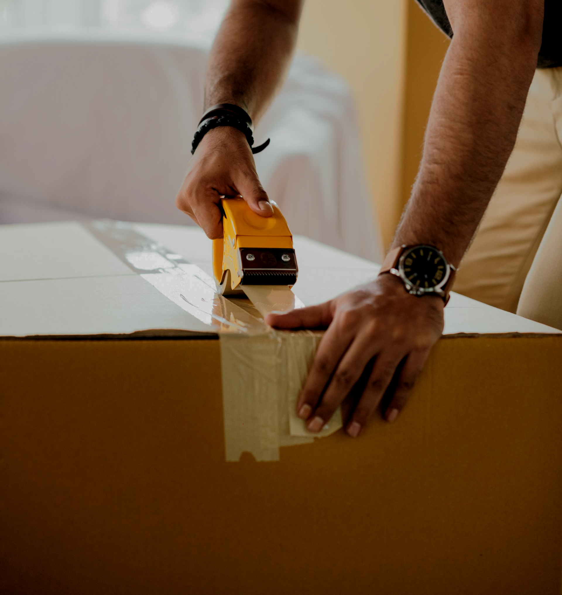 A man wearing a watch is wrapping a cardboard box with tape