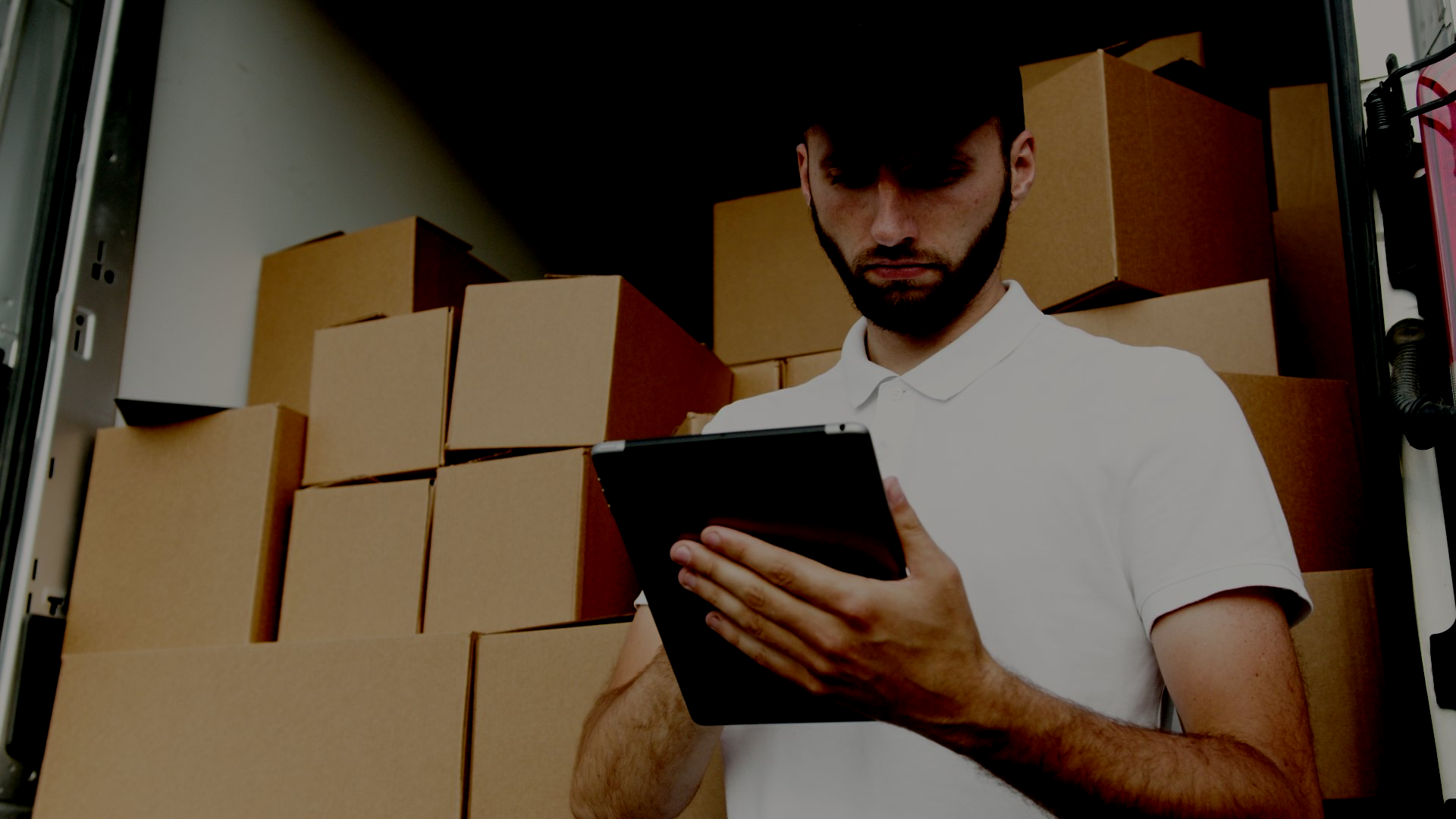 A man is using a tablet in front of a truck filled with cardboard boxes.