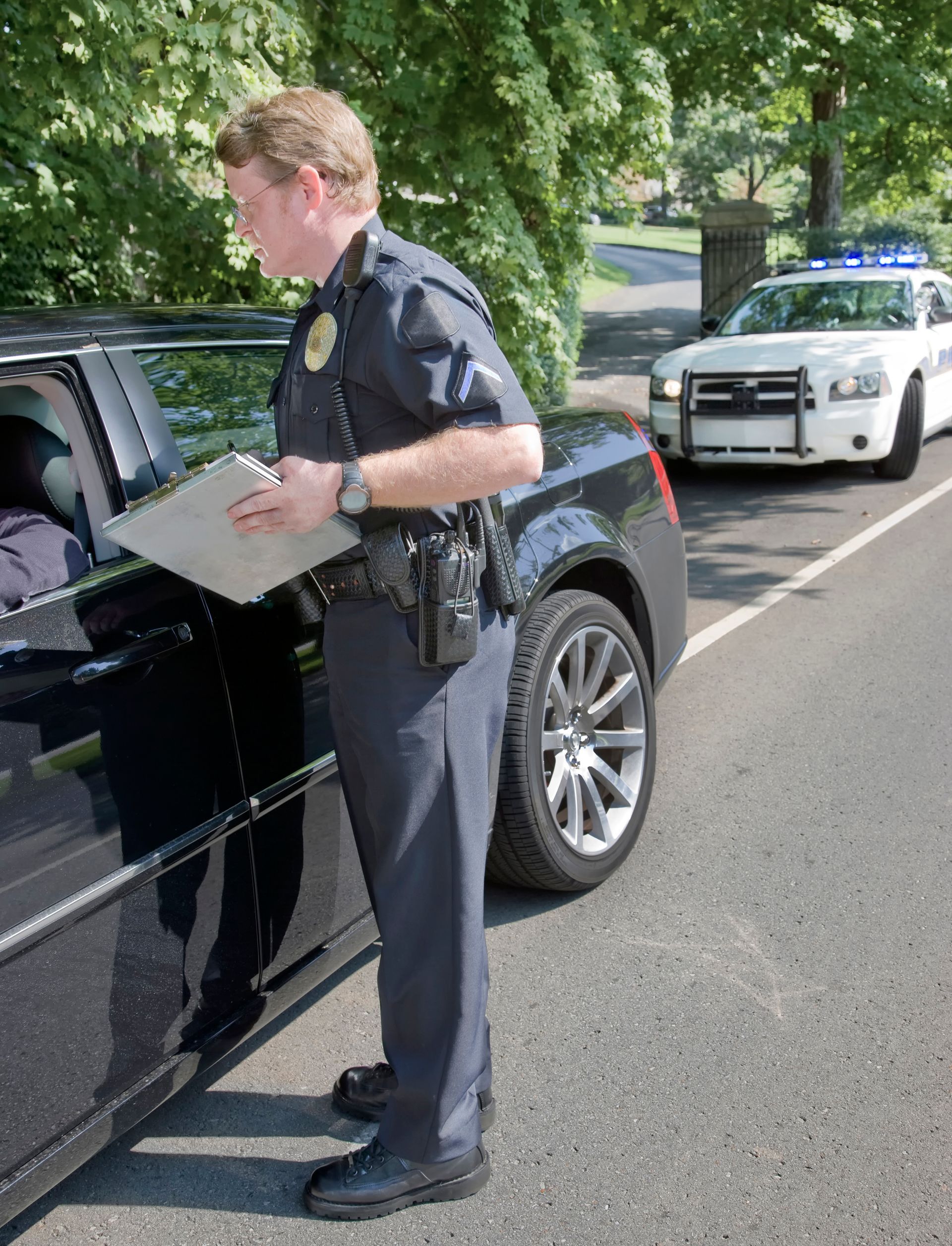 A police officer is standing next to a car holding a clipboard