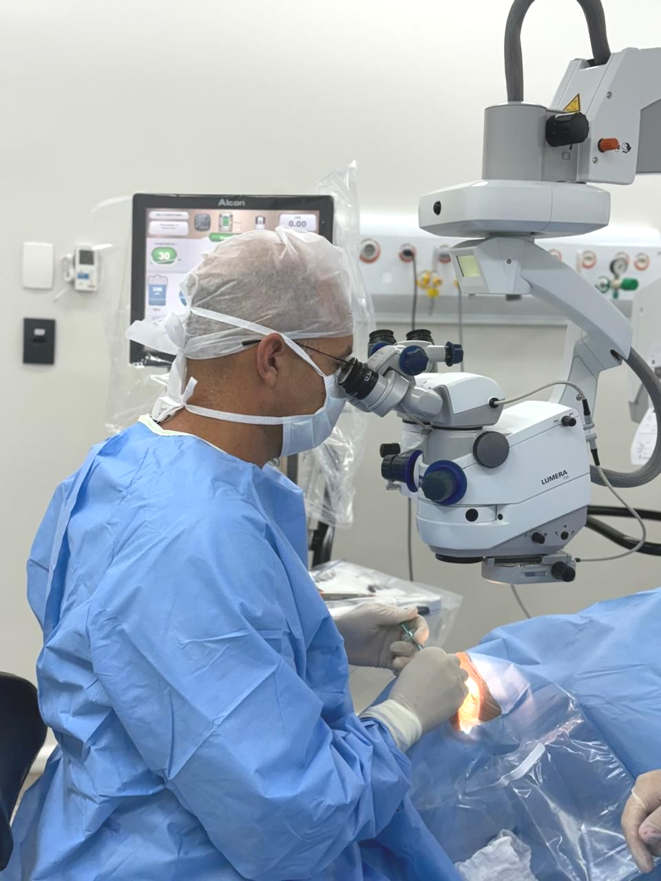 Mulher submetida a cirurgia ocular, olho iluminado, mãos enluvadas do médico. Cenário cirúrgico, tons de azul.