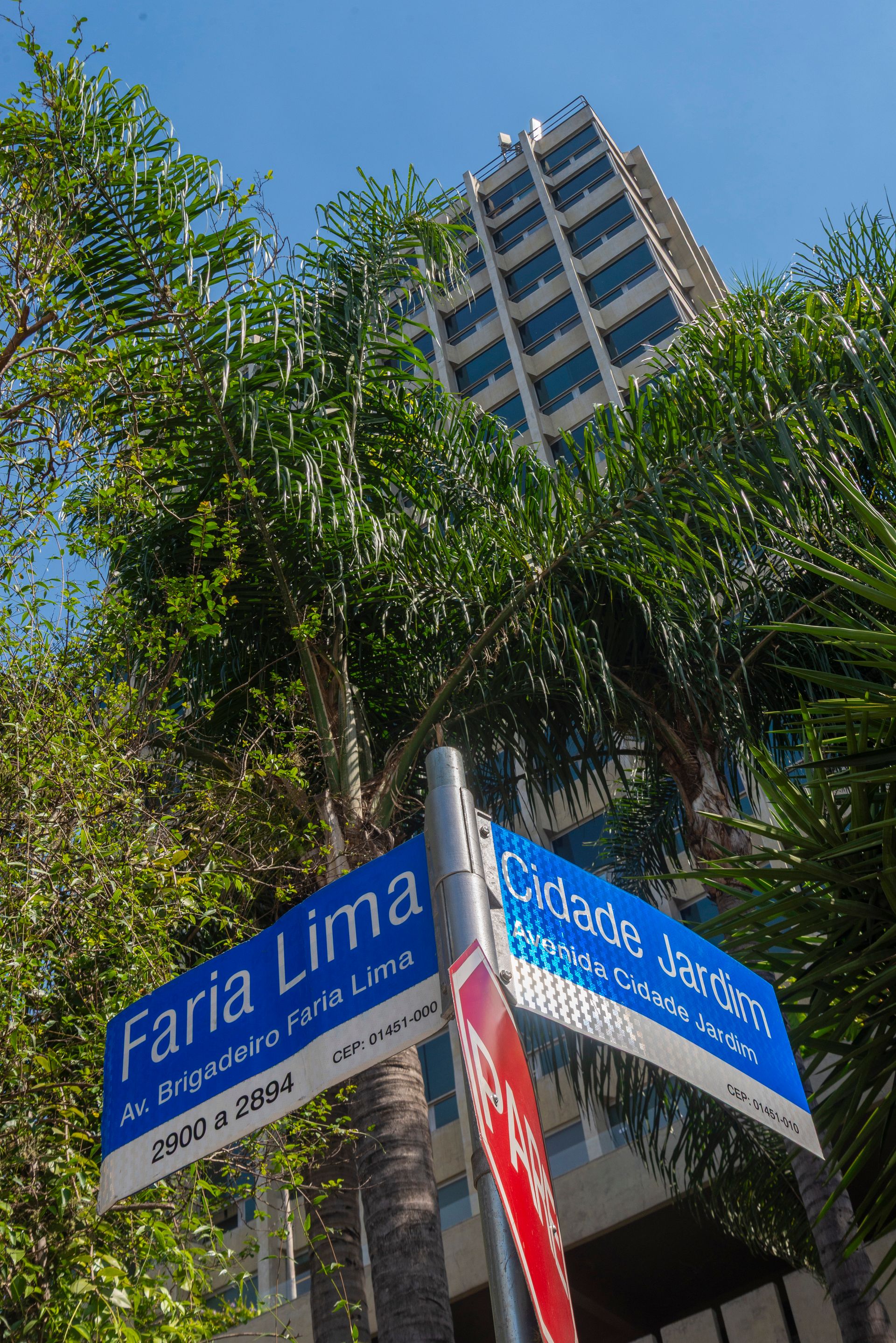 Placa de rua indicando Faria Lima e Cidade Jardim, com um prédio alto ao fundo.