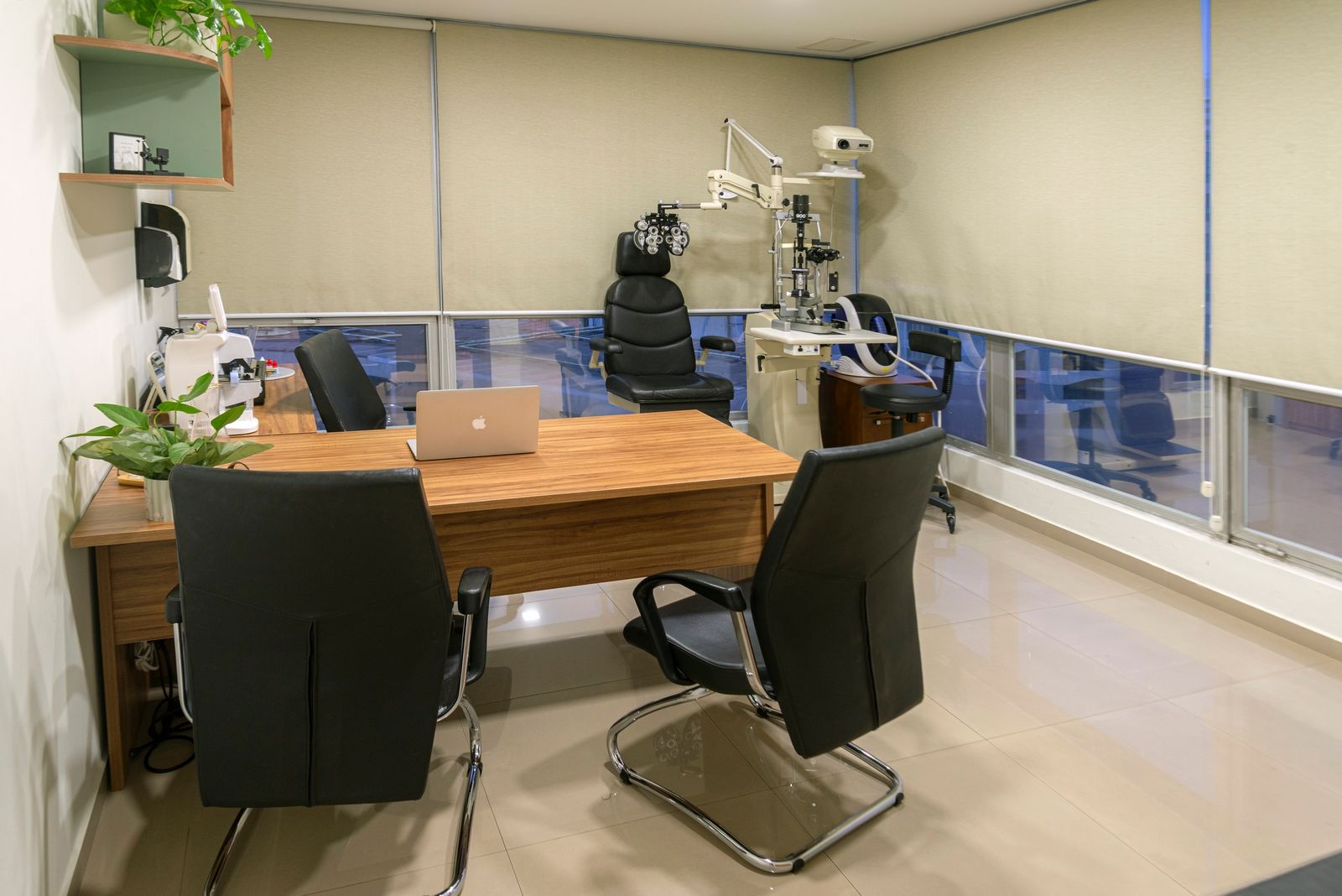 Consultório oftalmológico com equipamentos para exames, mesa e cadeiras. Tons neutros, luz natural.
