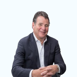 Smiling man in a dark blazer and white shirt seated against a light background