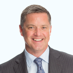 Portrait of a smiling man in a gray suit and blue tie against a light background