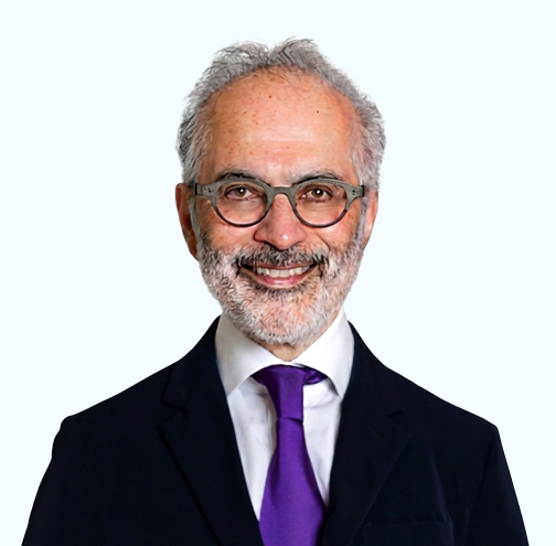 Studio portrait of a man in a black suit, white shirt, and dark tie, smiling against a light background