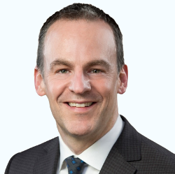 Studio headshot of a smiling man in a dark suit and tie against a light background