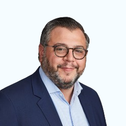Studio headshot of a man in glasses and a navy blazer against a white background
