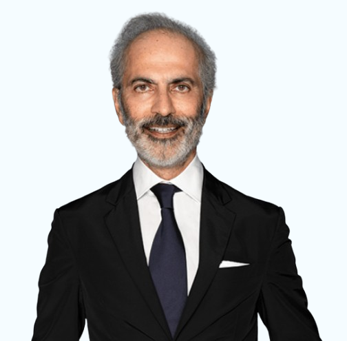 Studio portrait of a man in a black suit, white shirt, and dark tie, smiling against a light background